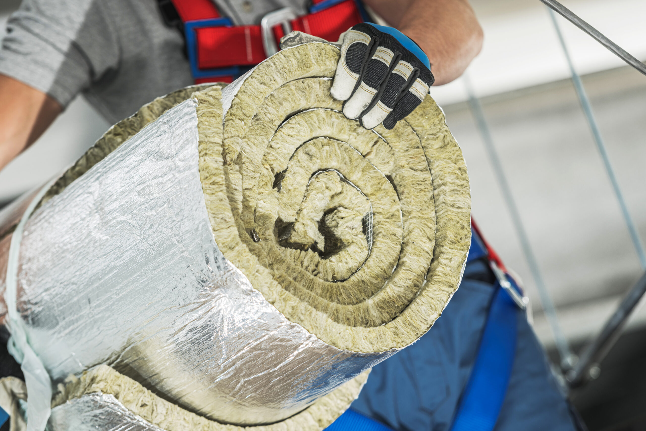 A construction worker holds rolled insulation material, preparing for installation. Safety gear is worn, highlighting the importance of worker safety on site.