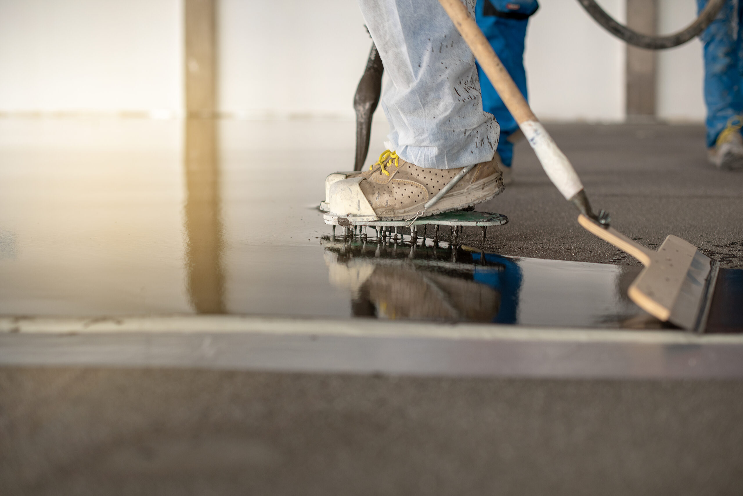 Worker working on the floor of an industrial building. Construction worker producing grout and finishing wet concrete floor.